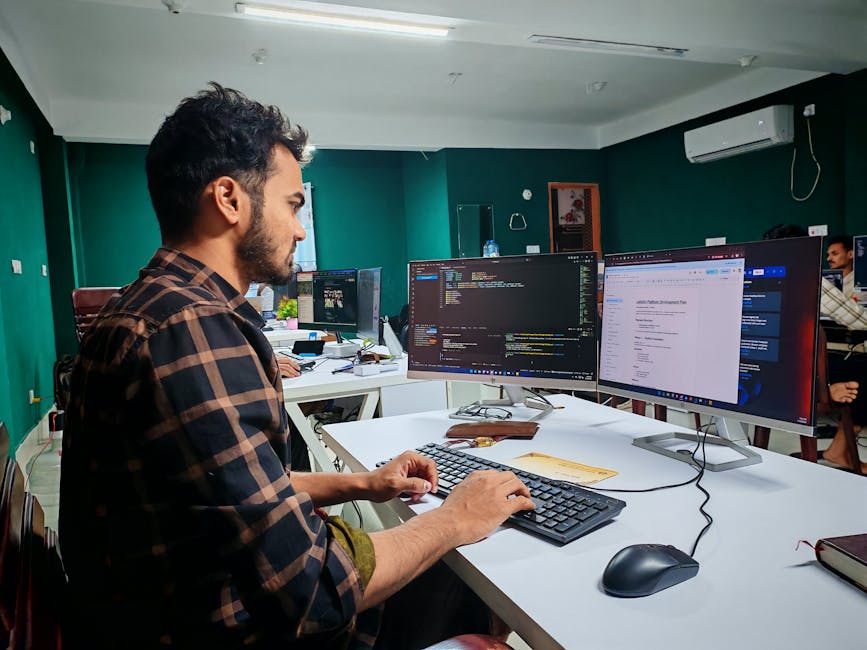A software developer working on code at a dual monitor setup