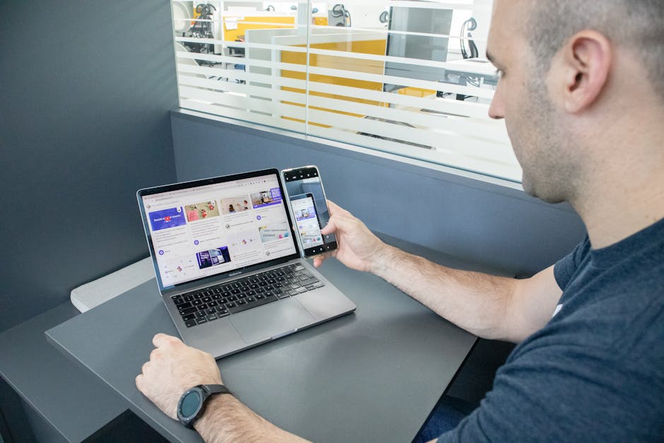 A man multitasking with a laptop and smartphone in an office